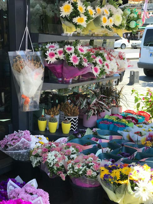 Display of fresh floral arrangements outside a florist shop, featuring a variety of colorful bouquets including white daisies with yellow centers, pink and white chrysanthemums, and yellow sunflowers.